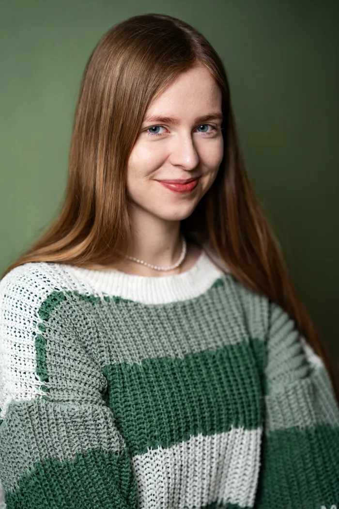Josefin Schäferhoff im grün-weiß gestreiften Strickpulli vor grüner Wand, verschmitztes Lächeln